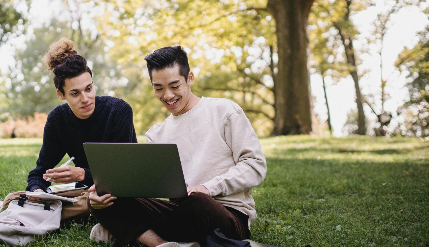 澳门威尼斯人网址学生看着笔记本电脑，在草坪上聊天.